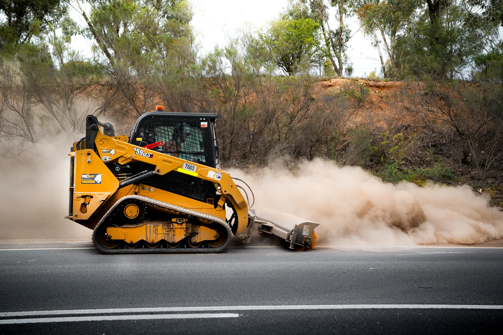 Skid steer sweeper clearing a roadside works area